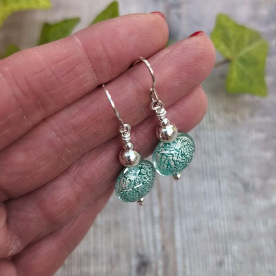 Video of green venetian glass silver earrings held in a hand, showing the silver pattern within the handmade green glass beads.