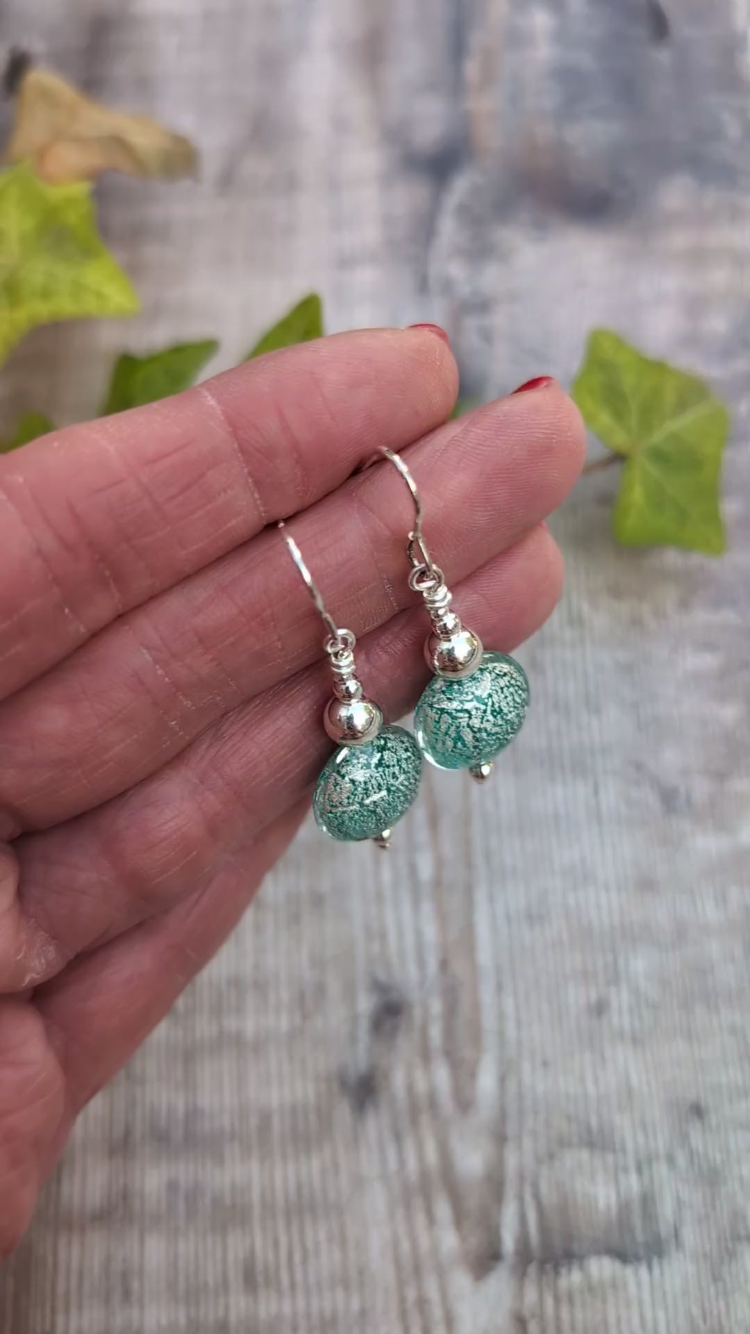 Video of green venetian glass silver earrings held in a hand, showing the silver pattern within the handmade green glass beads.