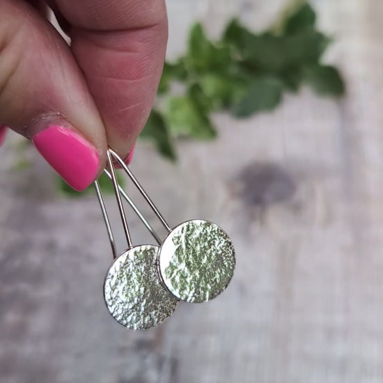 Video of Silver organic disc long earrings held up by their ear wires, showing the uneven organic texture on the recycled Sterling Silver discs.