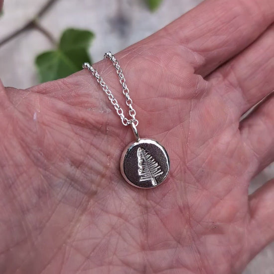Video of Silver evergreen tree necklace shown in a hand to show the size of the round recycled Sterling Silver pendant.