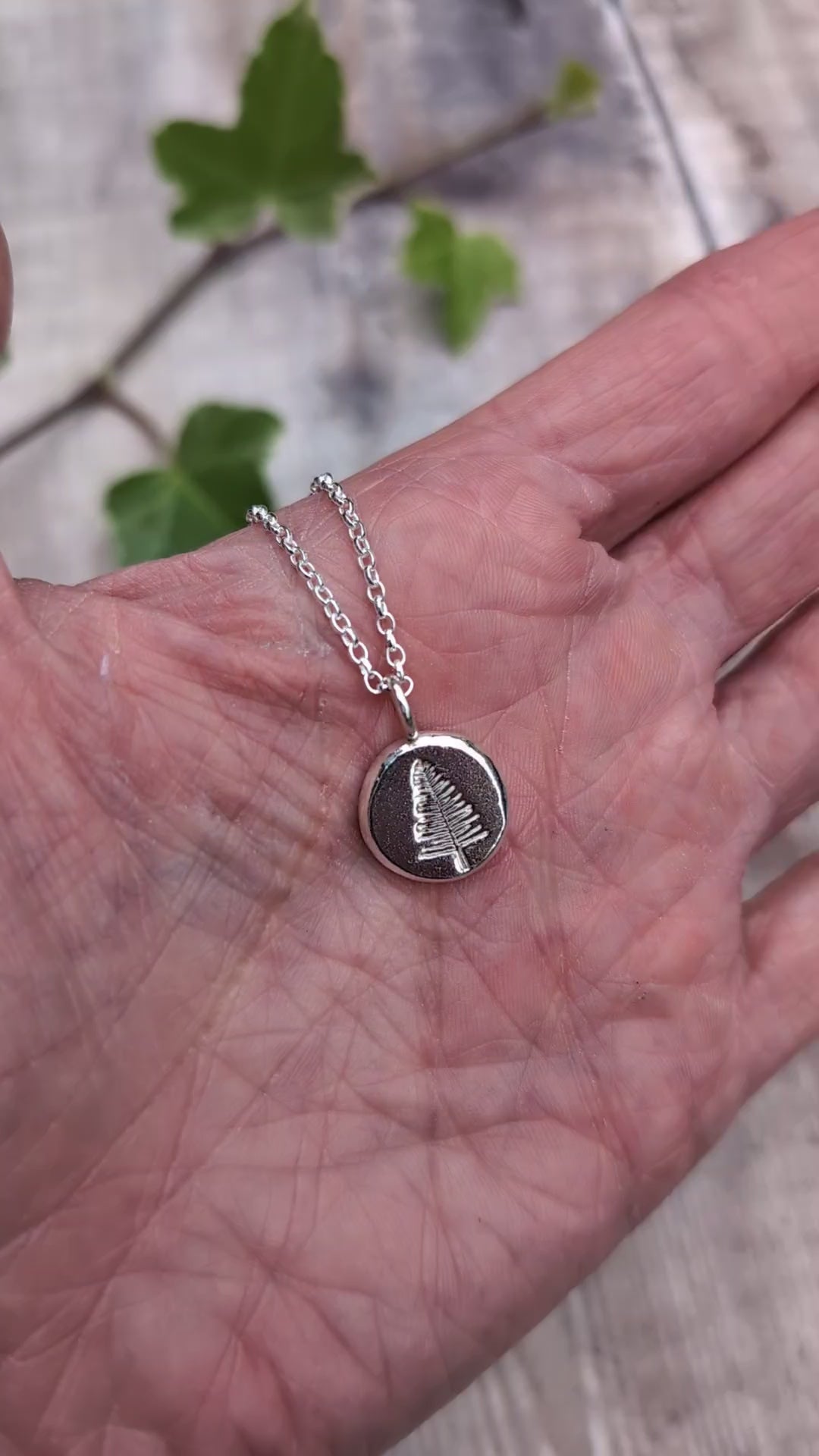 Video of Silver evergreen tree necklace shown in a hand to show the size of the round recycled Sterling Silver pendant.