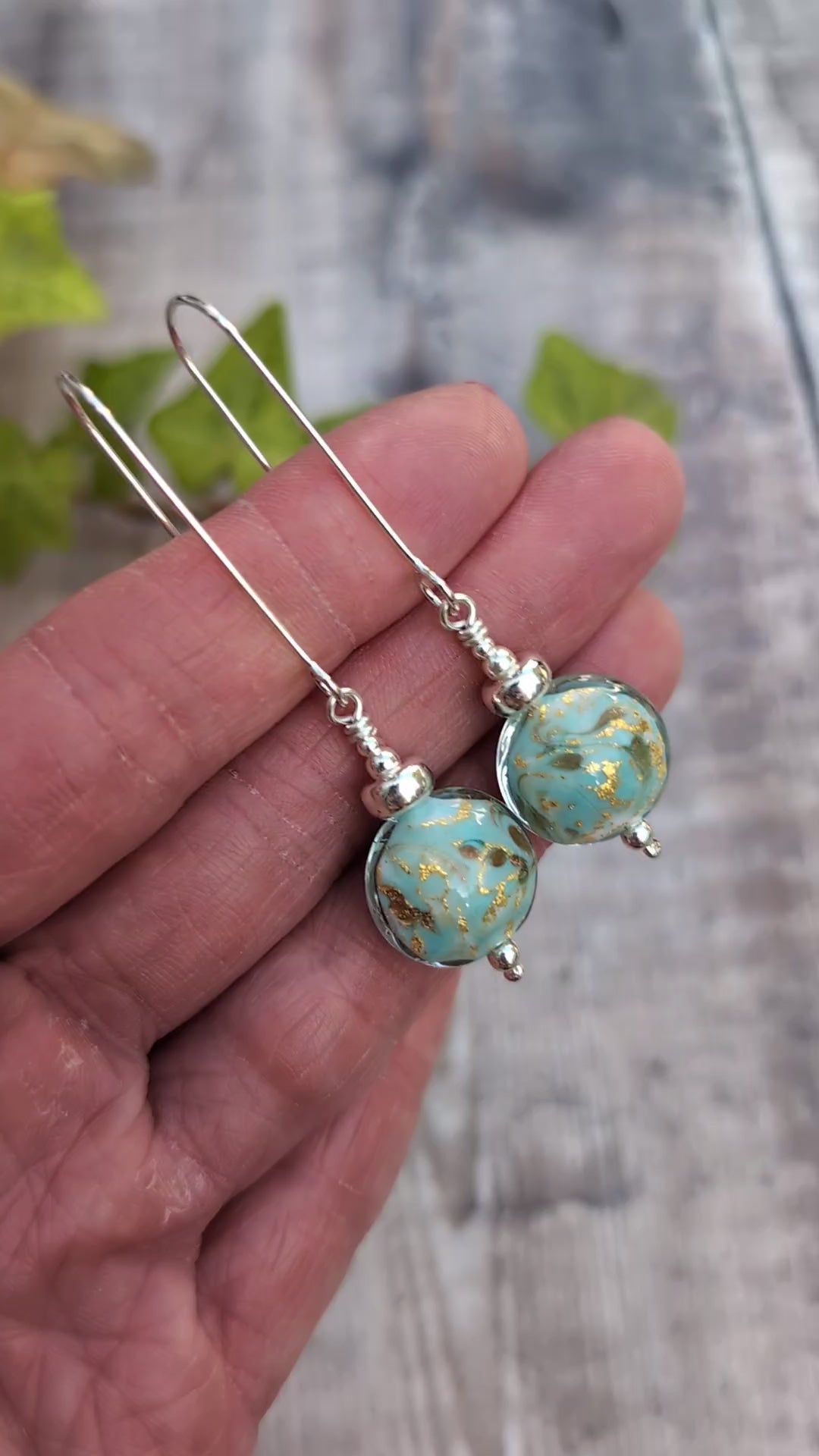 Video of Close up of turquoise marbled Venetian glass long silver earrings held in a hand, with turquoise blue and gold handmade lampwork glass beads.