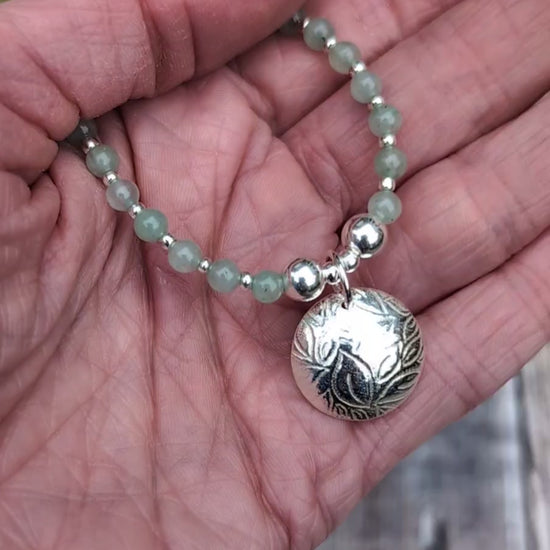 Video of Green Aventurine and Silver Leaf Disc Necklace held in the palm of a hand, showing the size of the textured silver disc charm and the pale green gemstone beads.