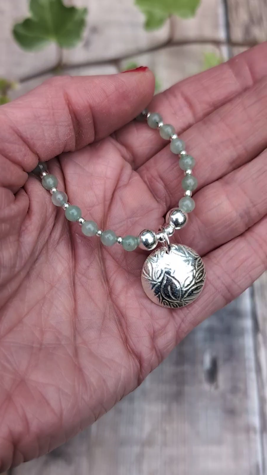 Video of Green Aventurine and Silver Leaf Disc Necklace held in the palm of a hand, showing the size of the textured silver disc charm and the pale green gemstone beads.