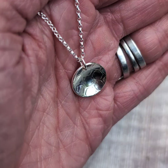 Video of a silver honeycomb disc necklace held in a hand, showing the detailed pattern pressed into the recycled Sterling Silver.