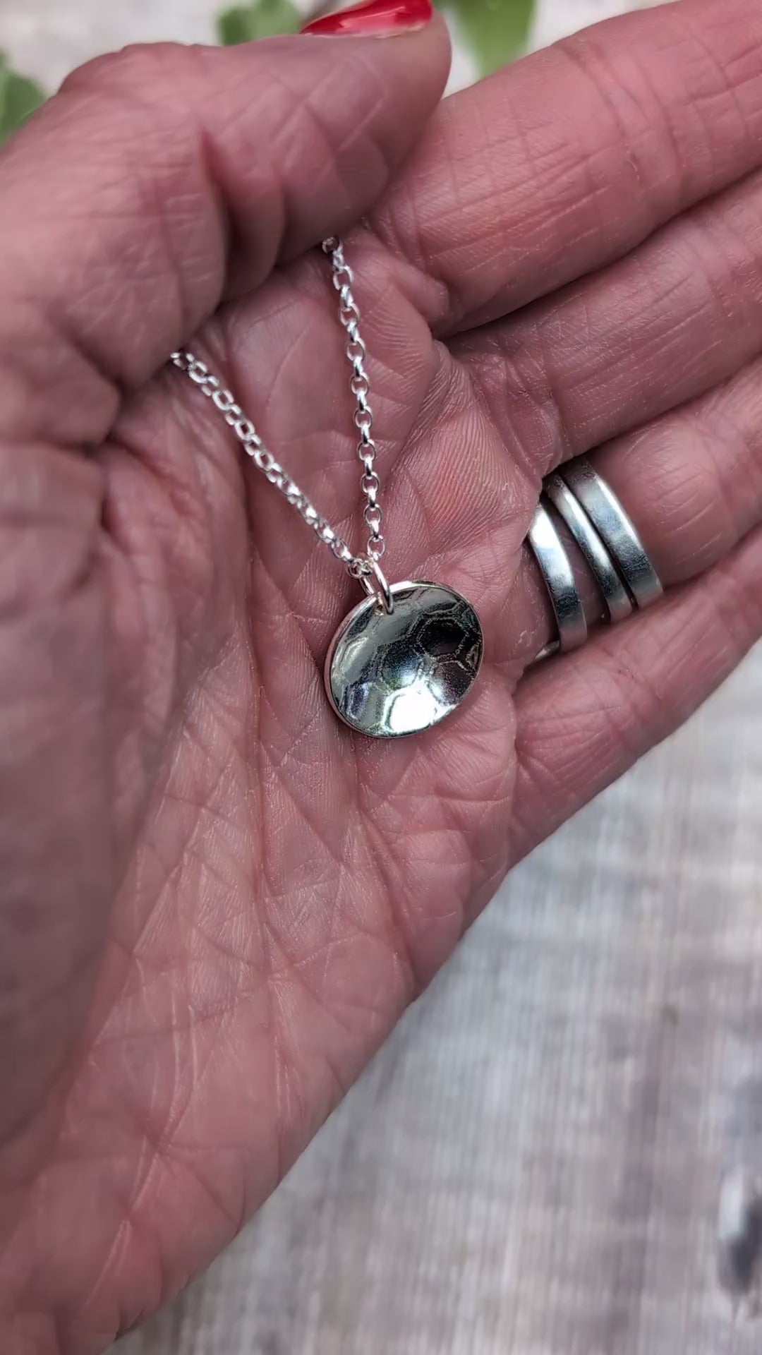 Video of a silver honeycomb disc necklace held in a hand, showing the detailed pattern pressed into the recycled Sterling Silver.