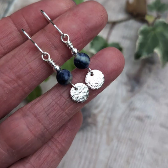 Video of blue sodalite and silver textured disc earrings resting on fingers, showing the natural blue and white patterns of the sodalite beads, textured sterling silver discs and silver bead details.