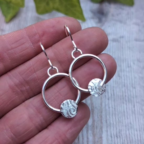 Close up of circle earring with textured disc handmade from recycled Sterling Silver held in a hand.