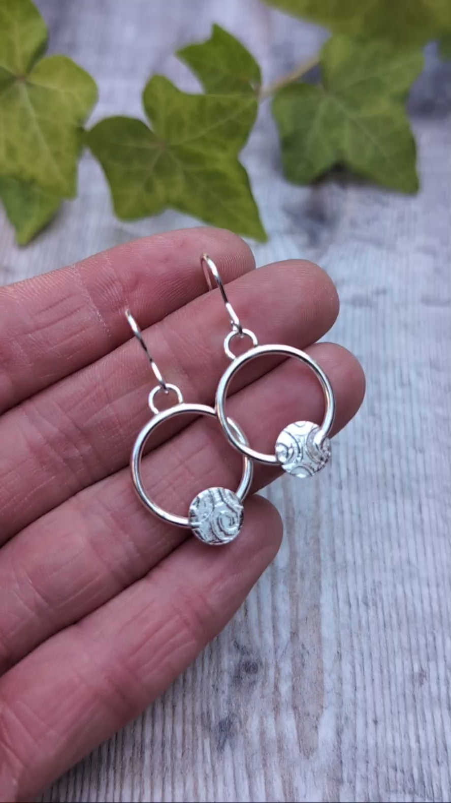 Close up of circle earring with textured disc handmade from recycled Sterling Silver held in a hand.