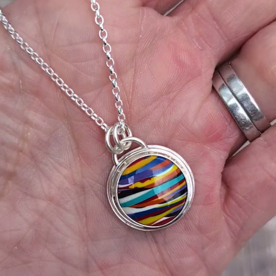 Video of Silver Multicoloured Surfite Round Necklace handmade from recycled Sterling Silver, with a colourful striped round Surfite stone, shown resting on a hand.