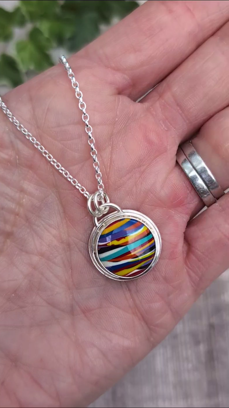 Video of Silver Multicoloured Surfite Round Necklace handmade from recycled Sterling Silver, with a colourful striped round Surfite stone, shown resting on a hand.