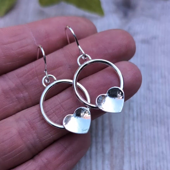 Circle earring with hammered hearts handmade from recycled Sterling Silver, shown resting on a hand to highlight the size and polished finish.