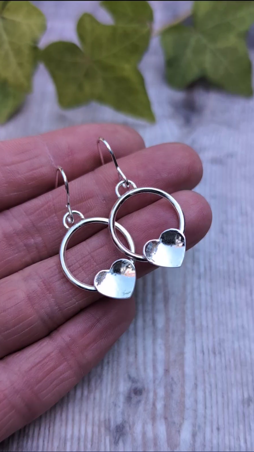 Circle earring with hammered hearts handmade from recycled Sterling Silver, shown resting on a hand to highlight the size and polished finish.