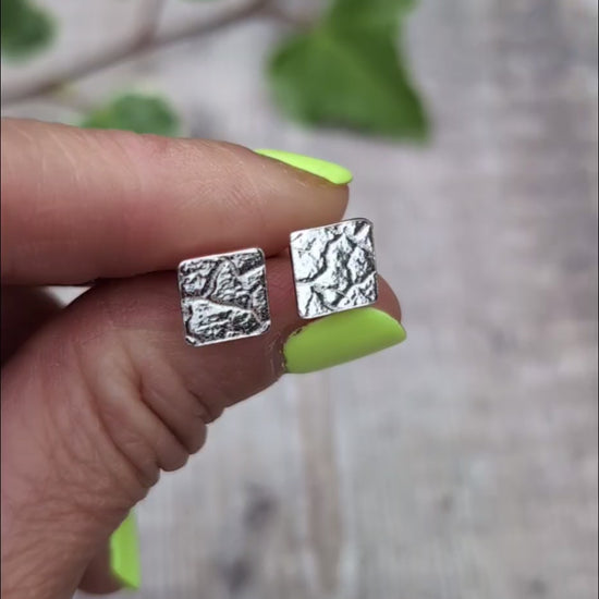 Video of Silver cracked earth pattern square stud earrings held on fingertips, showing their small square shape and textured silver surface.