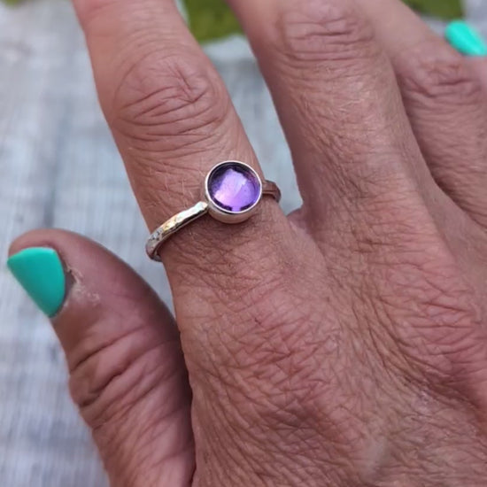 Amethyst ring size S handmade from recycled Sterling Silver, worn on a finger with the round purple Amethyst gemstone shown in natural light.