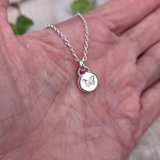 Video of Silver butterfly pebble necklace held in a hand, showing the size and hand stamped butterfly design on the small silver pendant.