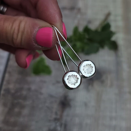 Video of silver daisy pebble long earrings held up close, showing the polished silver pebbles and hand stamped daisy design.