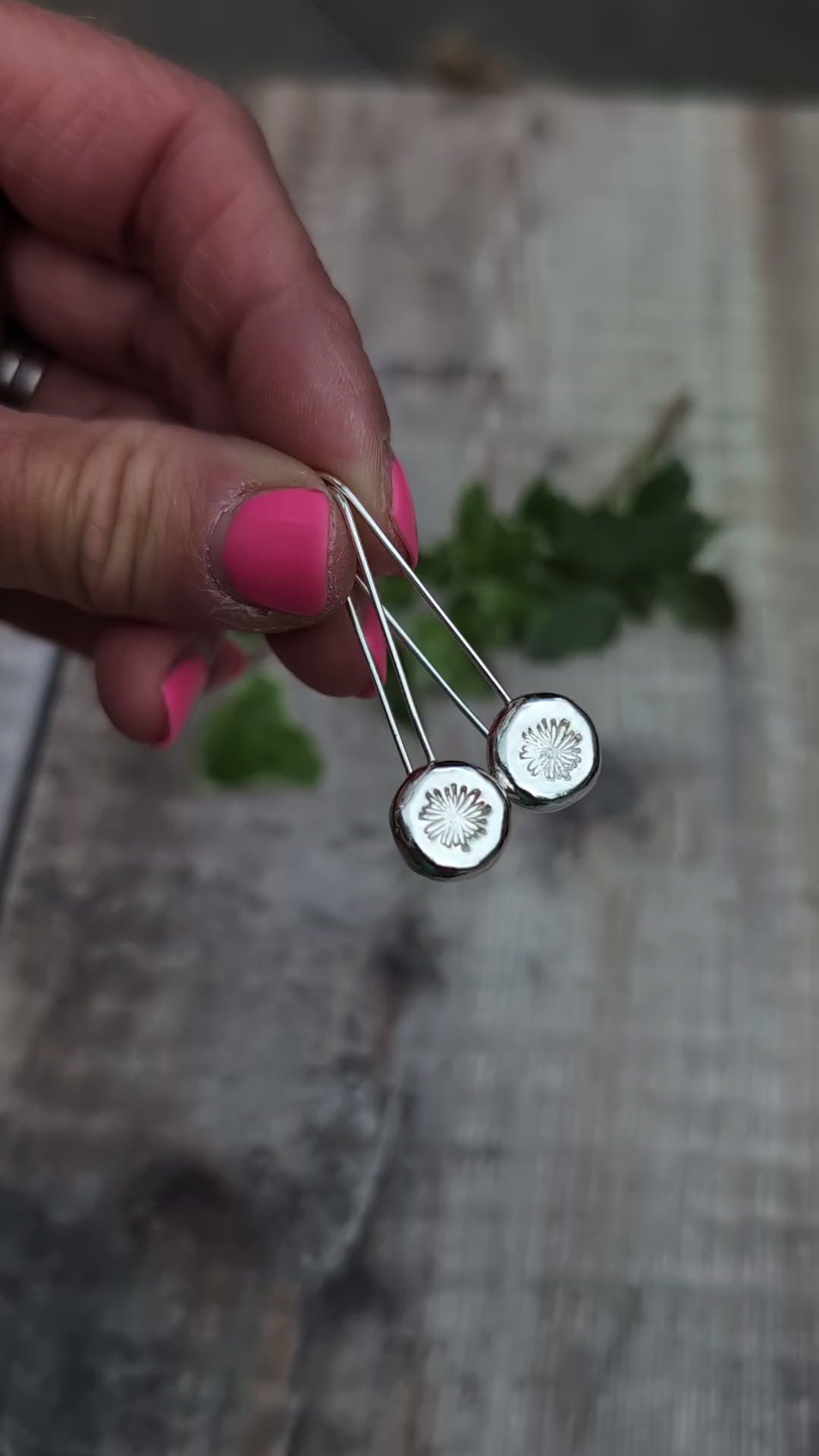 Video of silver daisy pebble long earrings held up close, showing the polished silver pebbles and hand stamped daisy design.