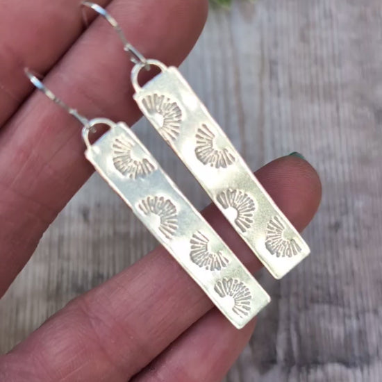 Video of Silver long rectangle sunrise earrings handmade from recycled Sterling Silver, held in a hand to show the long shape and hand stamped sunrise pattern.
