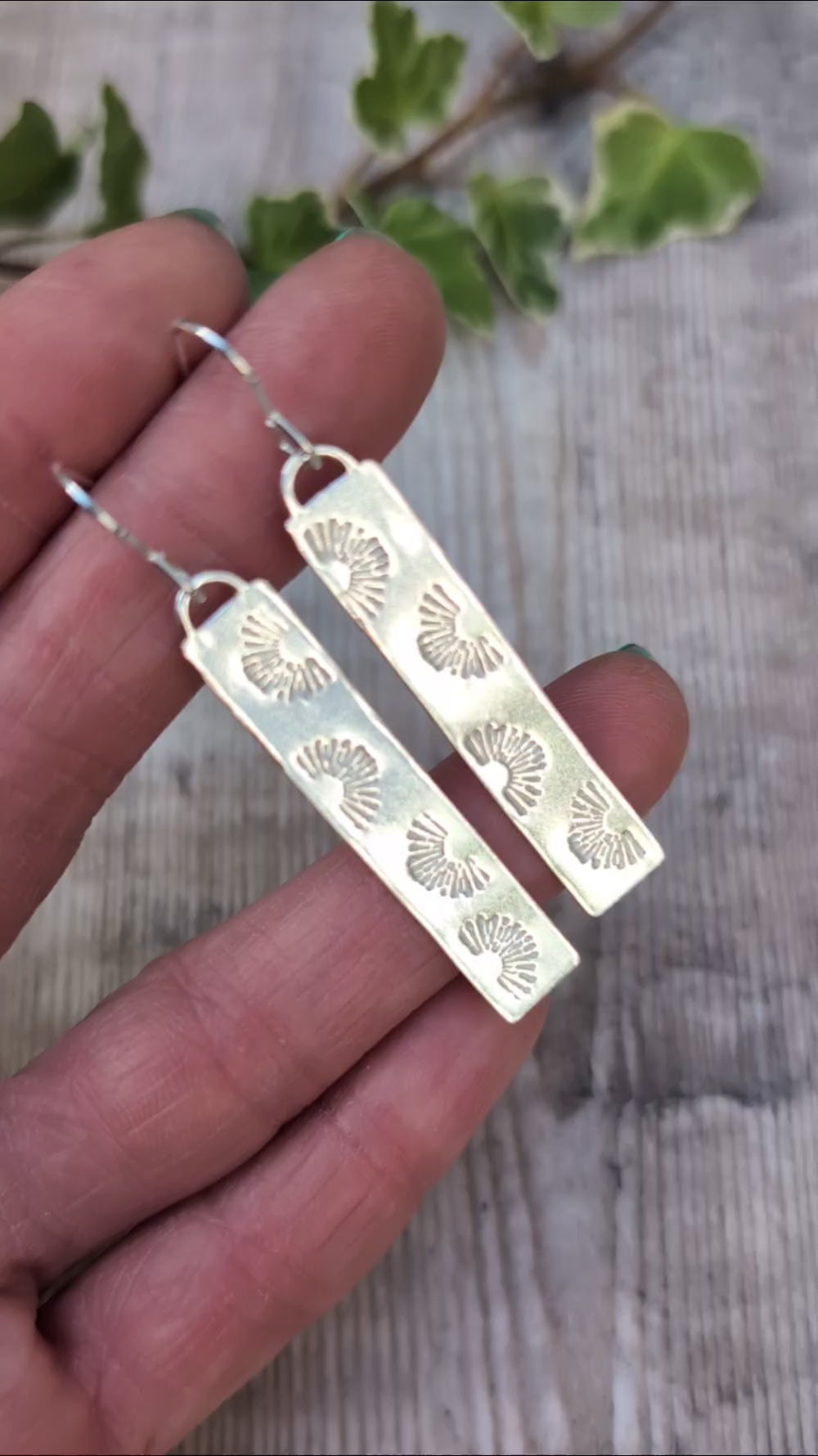 Video of Silver long rectangle sunrise earrings handmade from recycled Sterling Silver, held in a hand to show the long shape and hand stamped sunrise pattern.