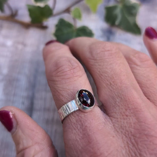 Video of Silver bark textured garnet ring worn on a finger, showing the oval dark red garnet gemstone set in polished silver and the textured band.