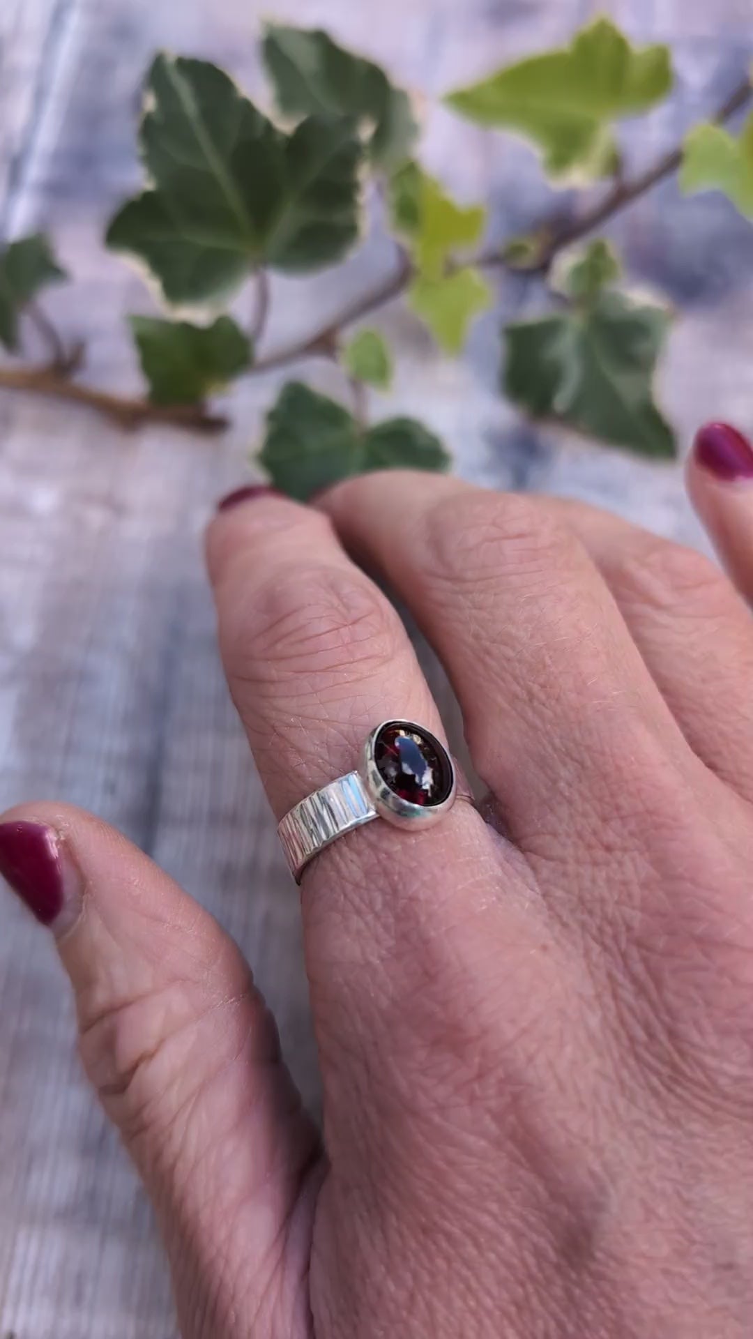 Video of Silver bark textured garnet ring worn on a finger, showing the oval dark red garnet gemstone set in polished silver and the textured band.