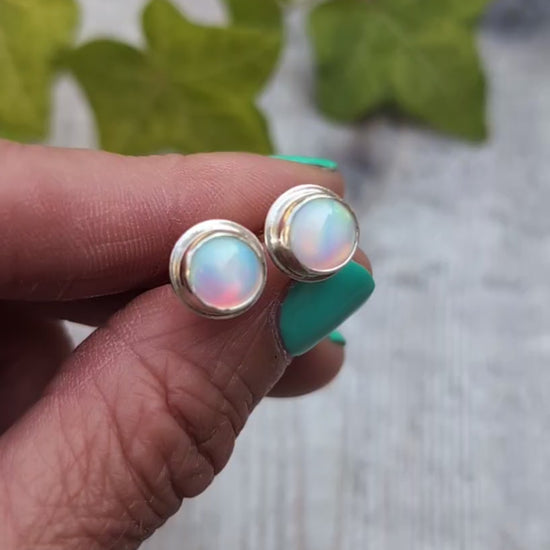 Close up of white aurora opal stud earrings handmade from recycled Sterling Silver, showing the soft flashes of pink, green and blue within the Aurora Opals.