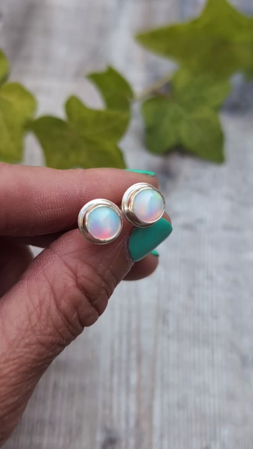 Close up of white aurora opal stud earrings handmade from recycled Sterling Silver, showing the soft flashes of pink, green and blue within the Aurora Opals.