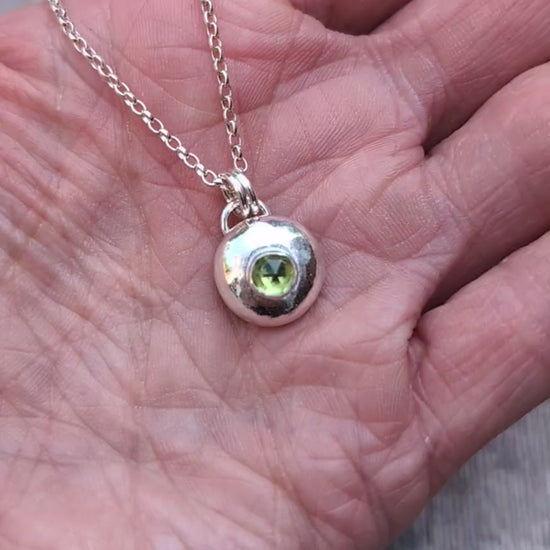 Peridot pebble necklace resting in the palm of a hand, showing the size of the handmade recycled Sterling Silver pebble pendant with a faceted Peridot gemstone.