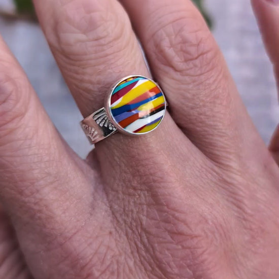Video of Silver sunrise surfite ring worn on a finger, showing the colourful round Surfite stone set in recycled sterling silver with a patterned band.