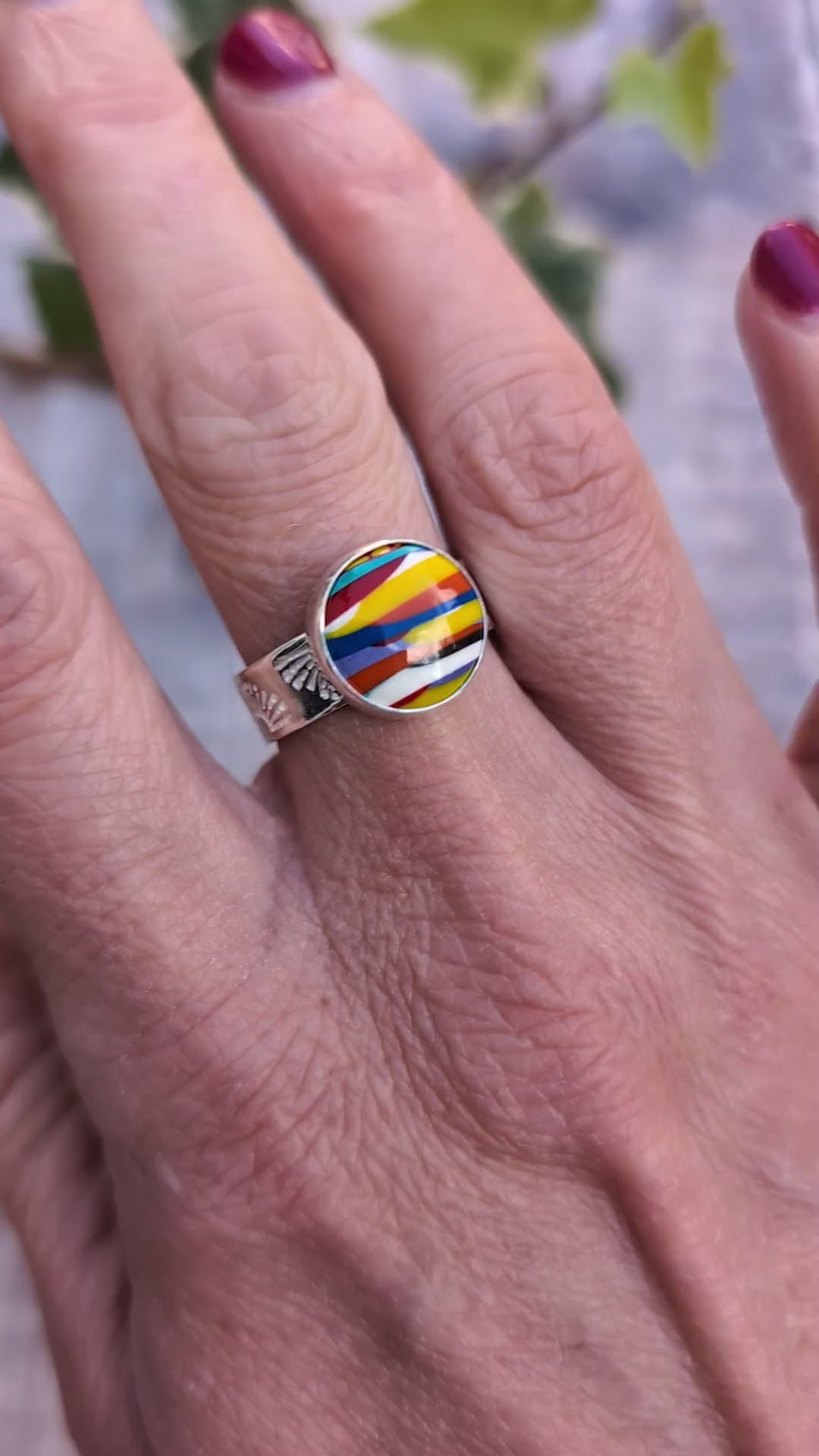 Video of Silver sunrise surfite ring worn on a finger, showing the colourful round Surfite stone set in recycled sterling silver with a patterned band.