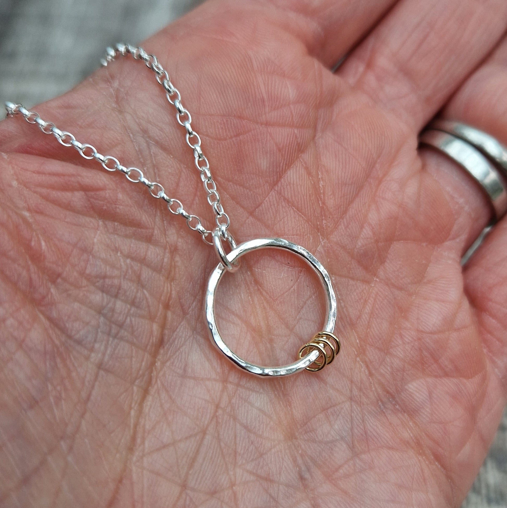 Each earring is a Sterling Silver hammered finish open circle suspended from silver earring wire. Three small gold open circles are threaded through the silver circle and move independently.