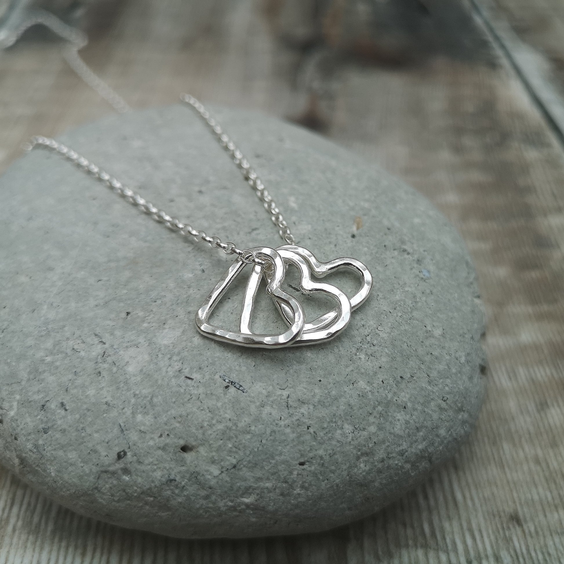 Silver chain threads through three silver open heart charms with hammered texture finish. Each charm moves independently along the chain.