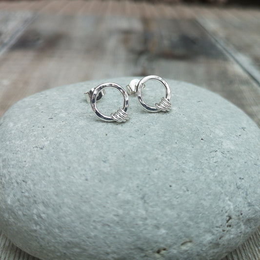 A pair of small silver circle stud earrings with four wrapped silver rings, displayed on a smooth stone surface, highlighting their minimalist and elegant design.