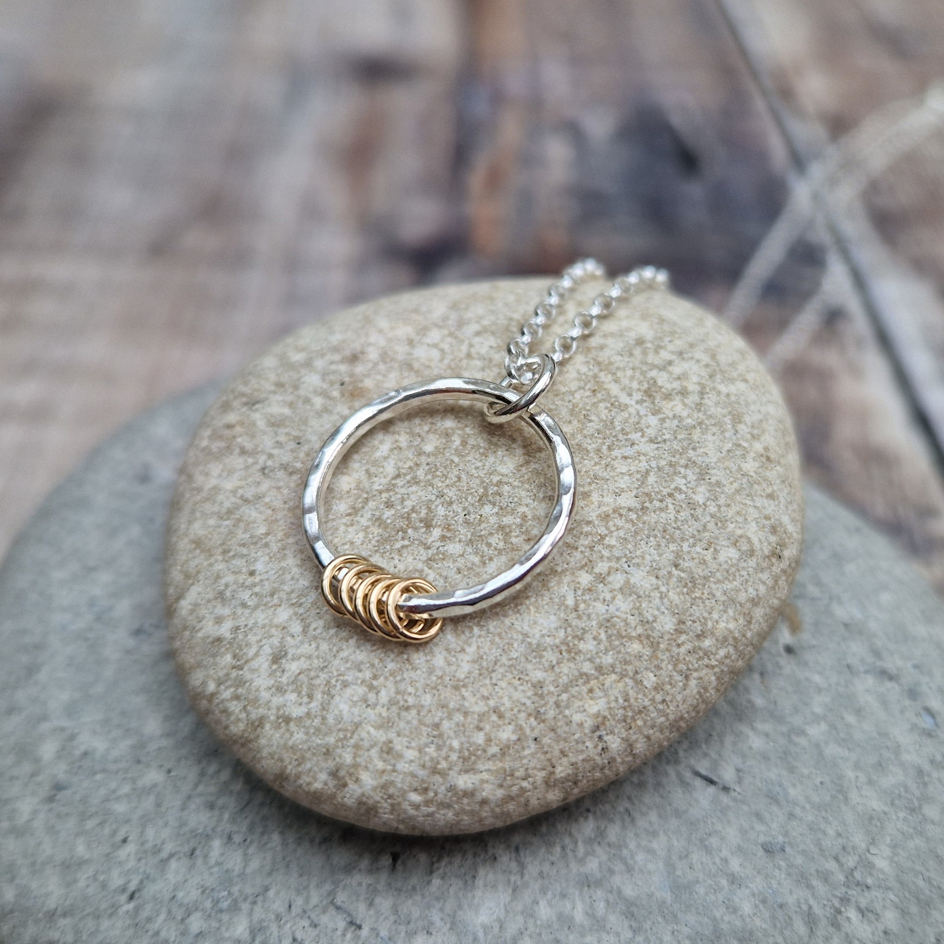 Pendant is a Sterling Silver hammered finish open circle suspended from silver chain via small silver circle link. Five small gold open circles are threaded through the silver circle and move independently.