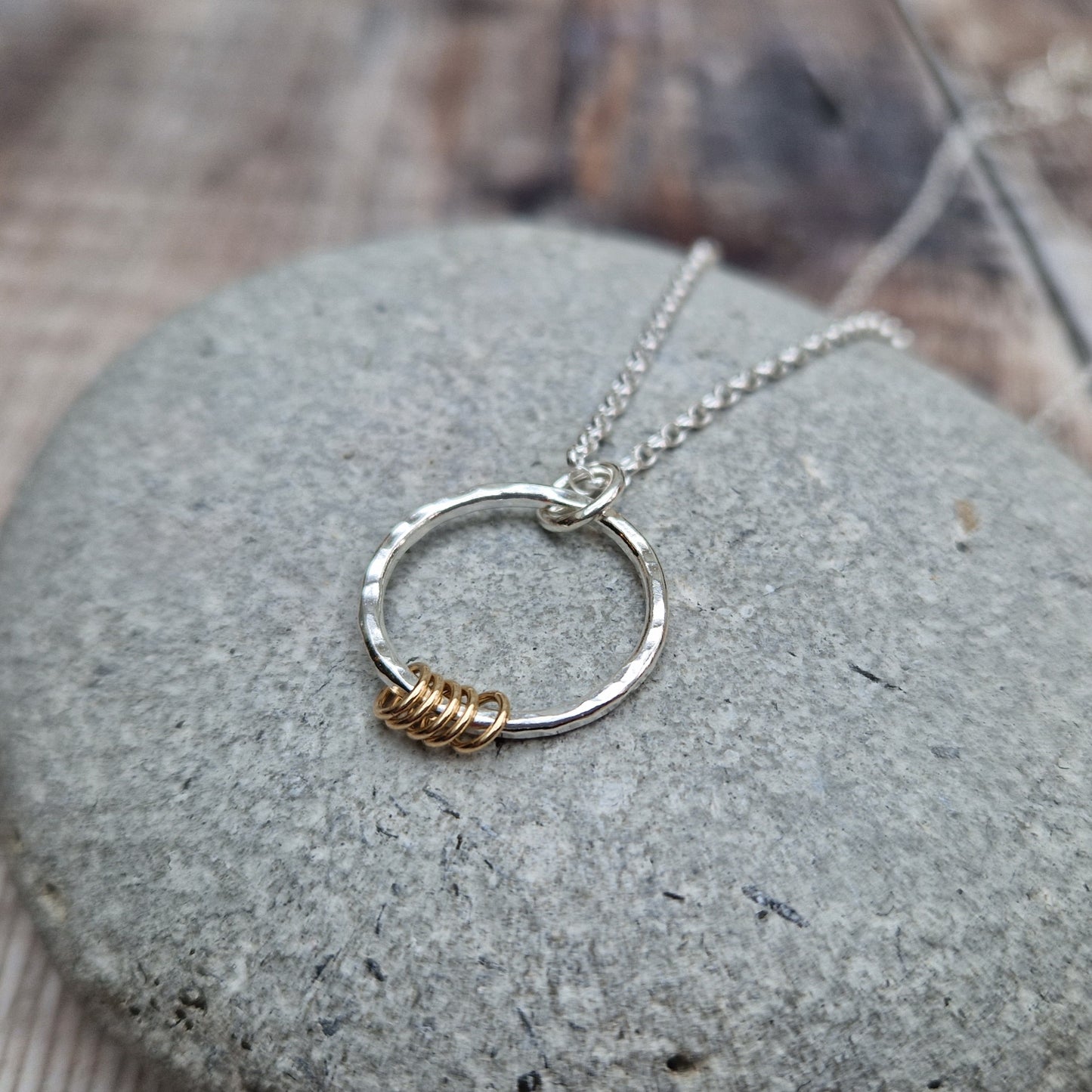 Pendant is a Sterling Silver hammered finish open circle suspended from silver chain via small silver circle link. Five small gold open circles are threaded through the silver circle and move independently.