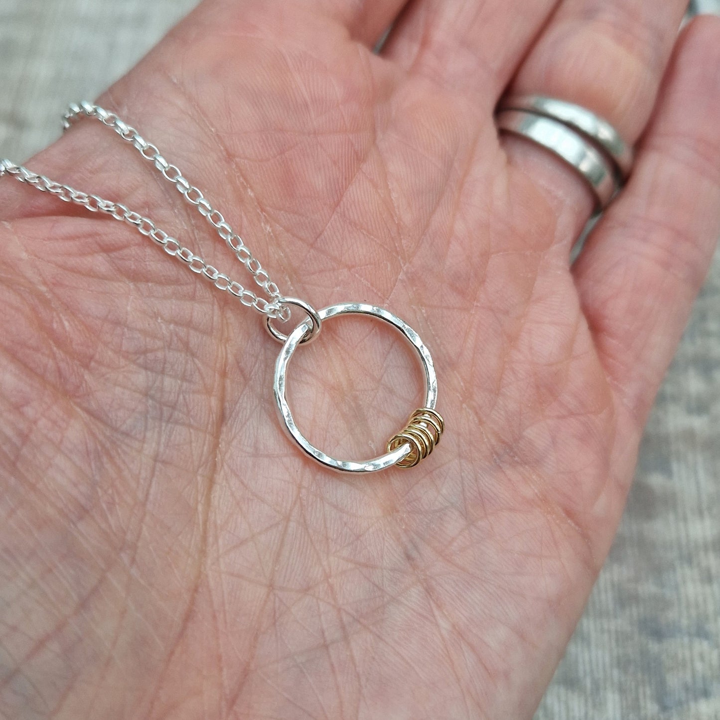 Pendant is a Sterling Silver hammered finish open circle suspended from silver chain via small silver circle link. Five small gold open circles are threaded through the silver circle and move independently.