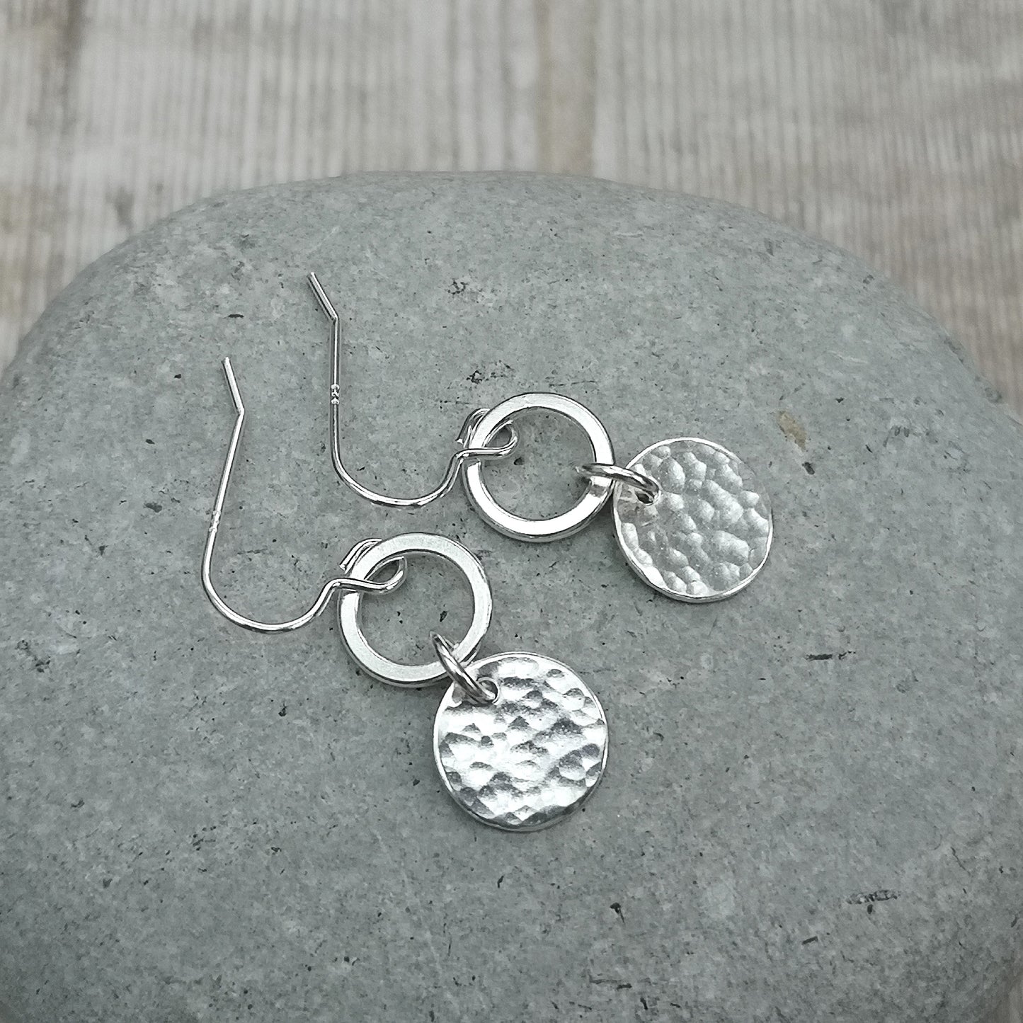 Each earring is a smooth silver open circle suspended from silver earring wire. Linked to the open circle via a small circle link is a hammered texture silver disc. Open circle to silver link to hammered silver disc.