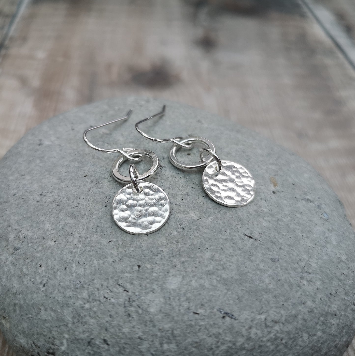 Each earring is a smooth silver open circle suspended from silver earring wire. Linked to the open circle via a small circle link is a hammered texture silver disc. Open circle to silver link to hammered silver disc.