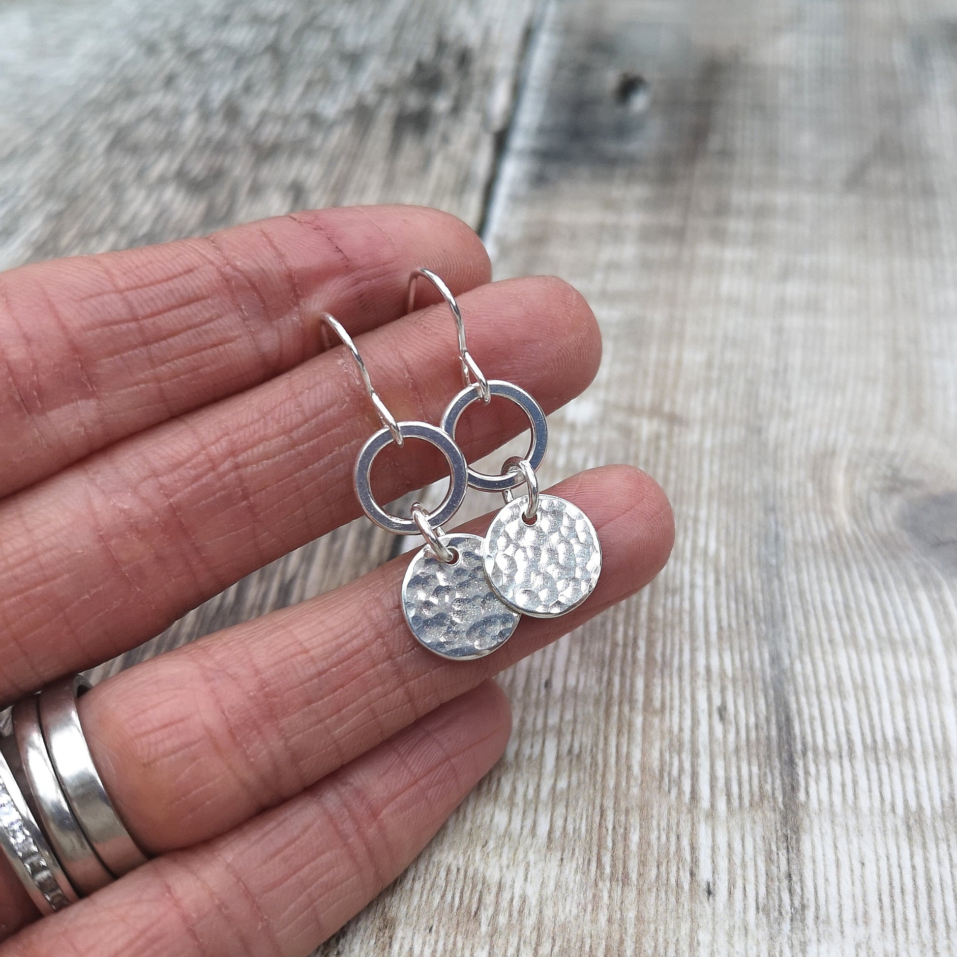 Each earring is a smooth silver open circle suspended from silver earring wire. Linked to the open circle via a small circle link is a hammered texture silver disc. Open circle to silver link to hammered silver disc.