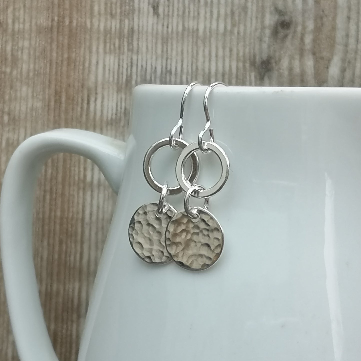 Each earring is a smooth silver open circle suspended from silver earring wire. Linked to the open circle via a small circle link is a hammered texture silver disc. Open circle to silver link to hammered silver disc.