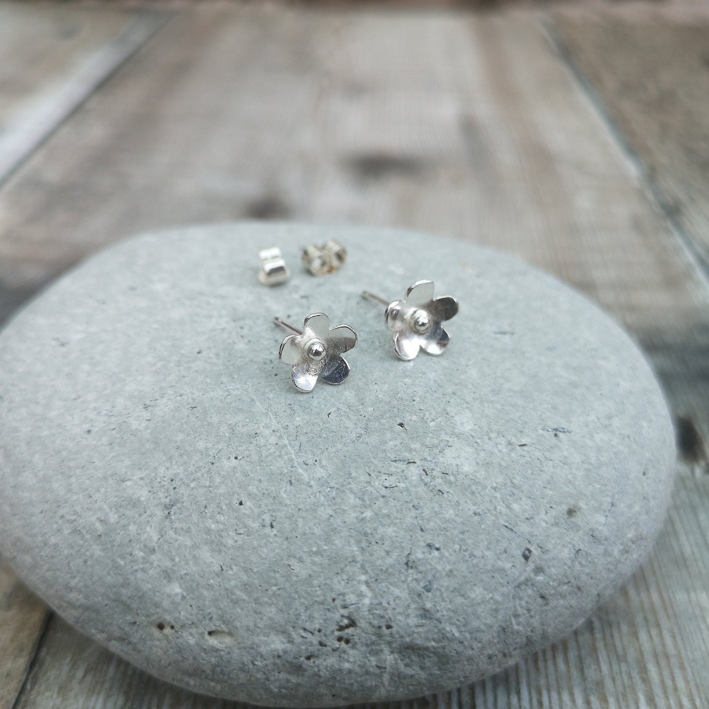 Each earring is a Sterling Silver five petal flower with petals slightly turned outwards with a central raised pistil. Mounted on a silver stud bar.