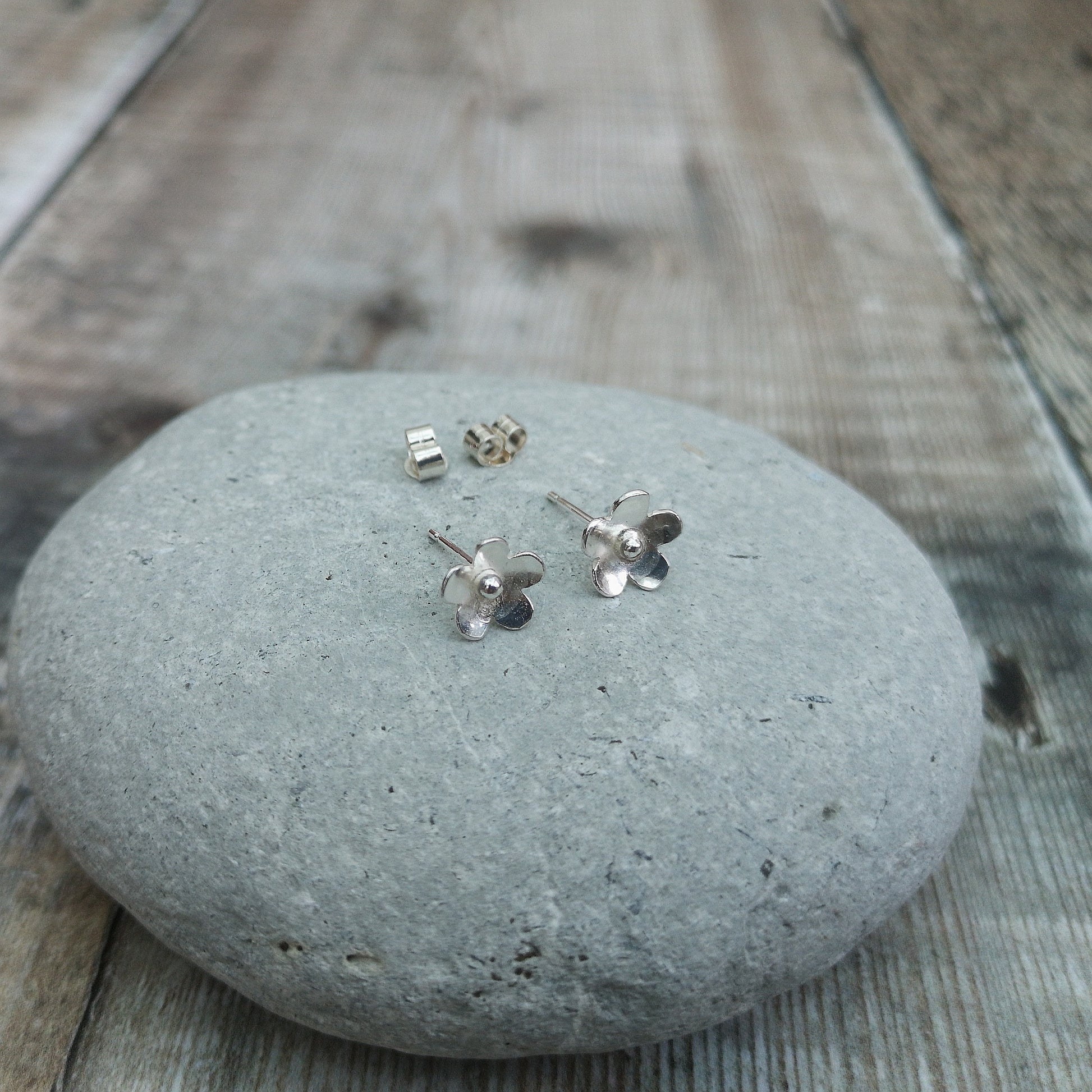 Each earring is a Sterling Silver five petal flower with petals slightly turned outwards with a central raised pistil. Mounted on a silver stud bar.