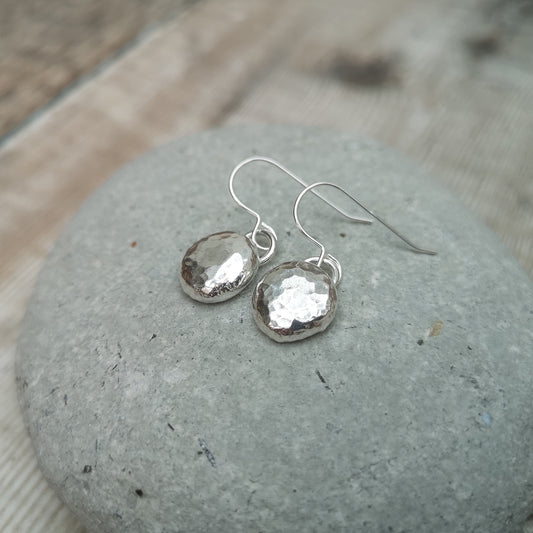 Each earring is a silver round pebble shape pendant with hammered texture finish suspended from a silver earring wire.