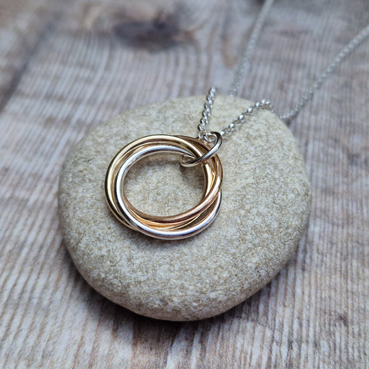 A detailed view of the Silver and Gold Three Linked Circle Necklace with intertwined gold and silver rings, resting on a smooth stone surface.