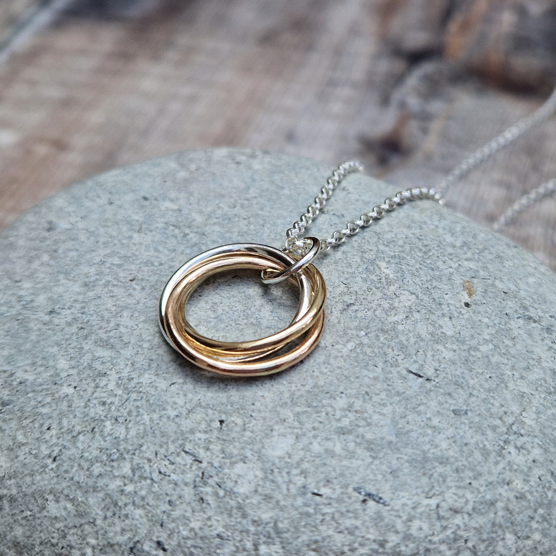 Silver and Gold Three Linked Circle Necklace. Three open circles, approximately 22mm in diameter, linked together as a Russian Ring (rings entwined). One circle is Sterling Silver, one is 9ct yellow gold and one is 9ct red gold. The pendant hangs from a silver necklace via a silver link.