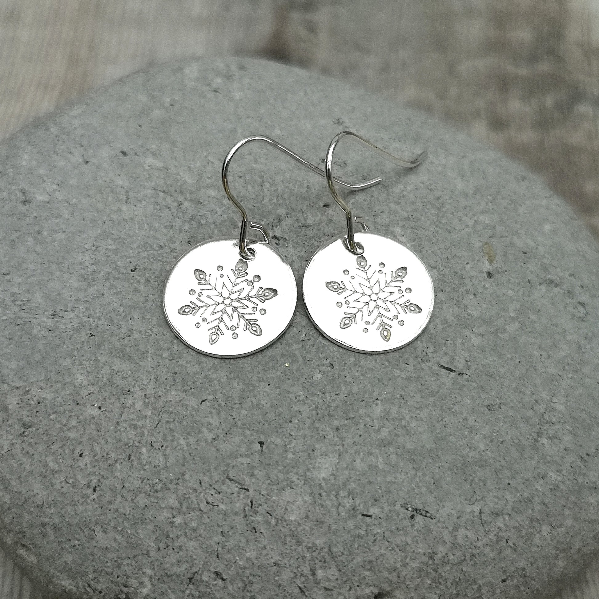 Each earring is a smooth silver disc shape stamped with one snowflake, suspended from silver earring wire.