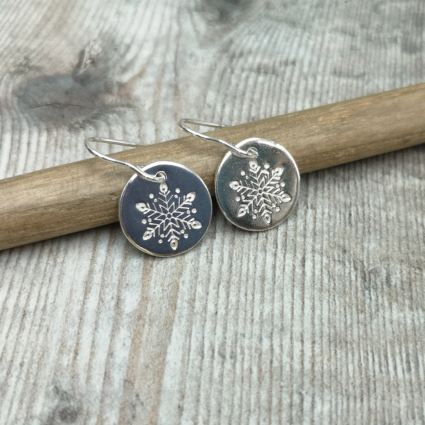 Each earring is a smooth silver disc shape stamped with one snowflake, suspended from silver earring wire.