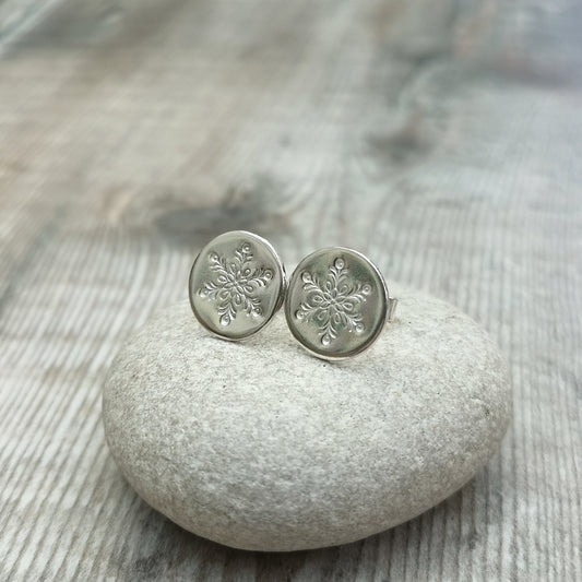 Each earring is a smooth silver disc shape stamped with one snowflake mounted onto a silver stud bar.