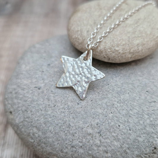 Pendant is a silver five-pointed flat star shape with hammered texture finish suspended from silver chain via a small open circle link.